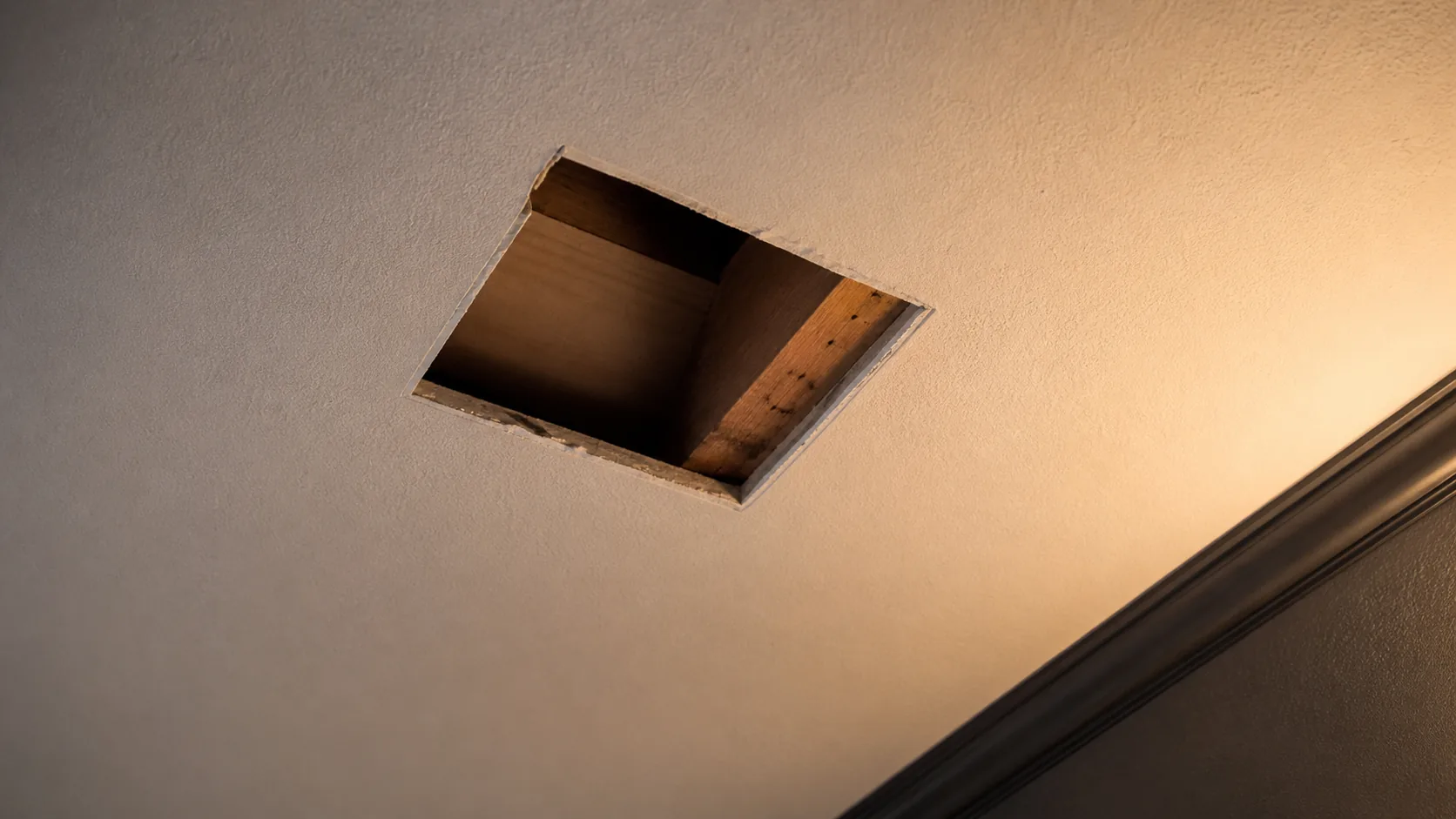 Finished textured ceiling with one localized drywall opening and warm side lighting.
